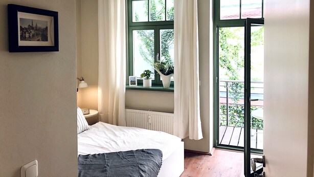 A bedroom with a bed, a bedside table, a hanging light, a window with curtains, and a view of greenery outside.
