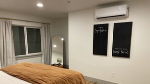 Un dormitorio con una cama, aire acondicionado, un espejo y dos carteles con mensajes motivacionales en la pared.