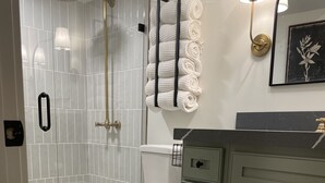 Un baño con inodoro, ducha con puerta de vidrio, toallero y lavabo con gabinete.