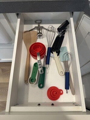 Eine Küchenschublade mit verschiedenen Küchenutensilien, darunter Schneebesen, Reibe und Messbecher.