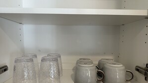 Una repisa con tazas de vidrio transparente y tazas de cerámica con asa.