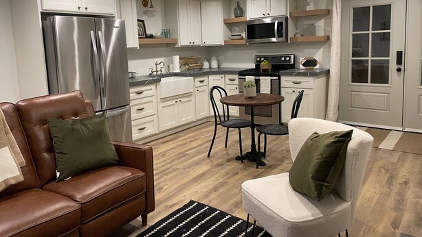 Una cocina moderna con armarios blancos, electrodomésticos de acero inoxidable y una zona de comedor con mesa y sillas.