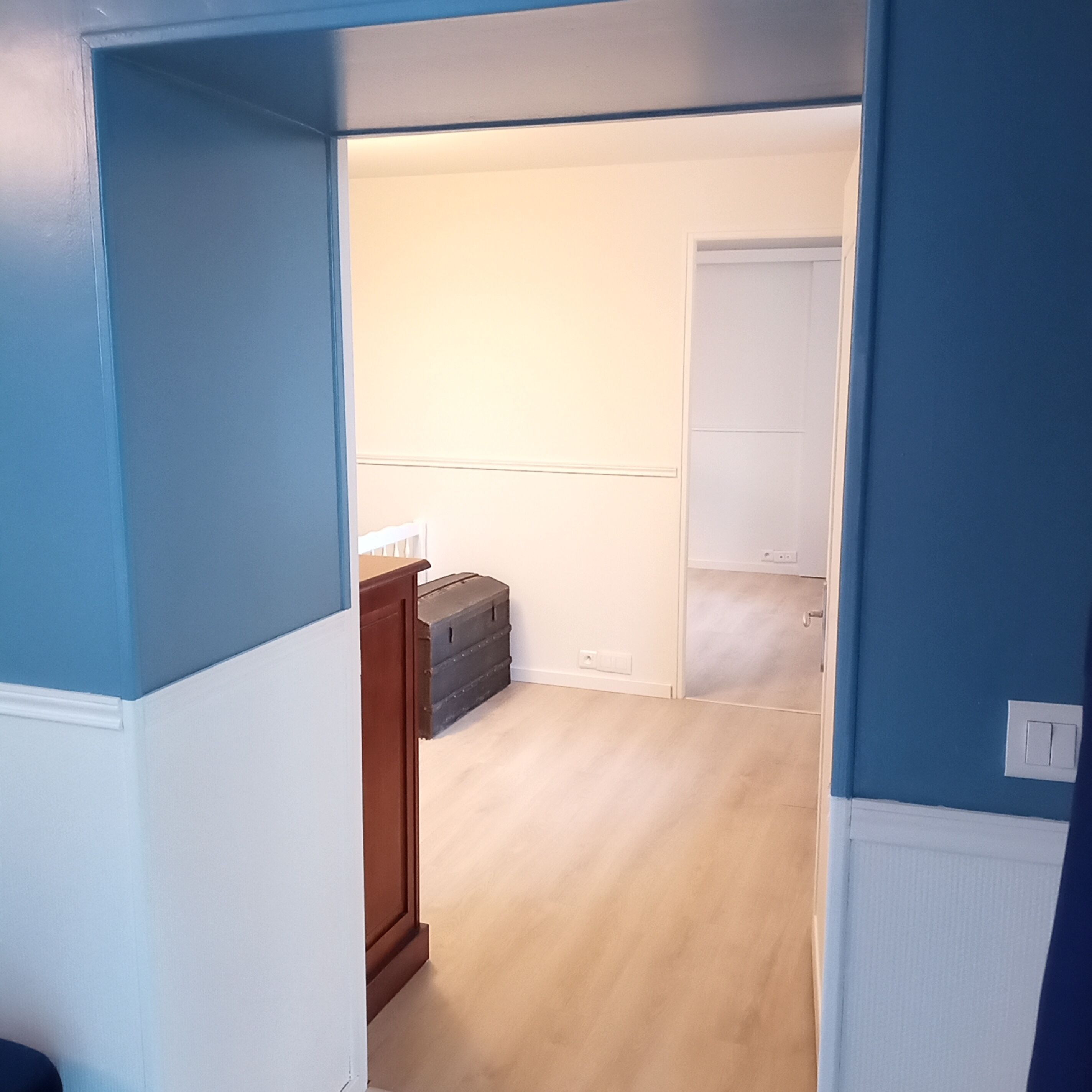 A hallway with a wooden cabinet, a light switch, and a door leading to another room.