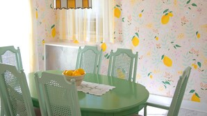 A dining area with a green table and chairs, a fruit-patterned wallpaper, a hanging lantern, and a wall clock. - Just a few blocks from Lake Erie!  4 season home with a cozy cottagey feel. (Lakeside Marblehead)