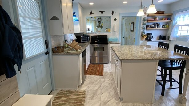 A modern kitchen with white cabinets, a central island, stainless steel appliances, and a brown rug. - Just a few blocks from Lake Erie!  4 season home with a cozy cottagey feel. (Lakeside Marblehead)