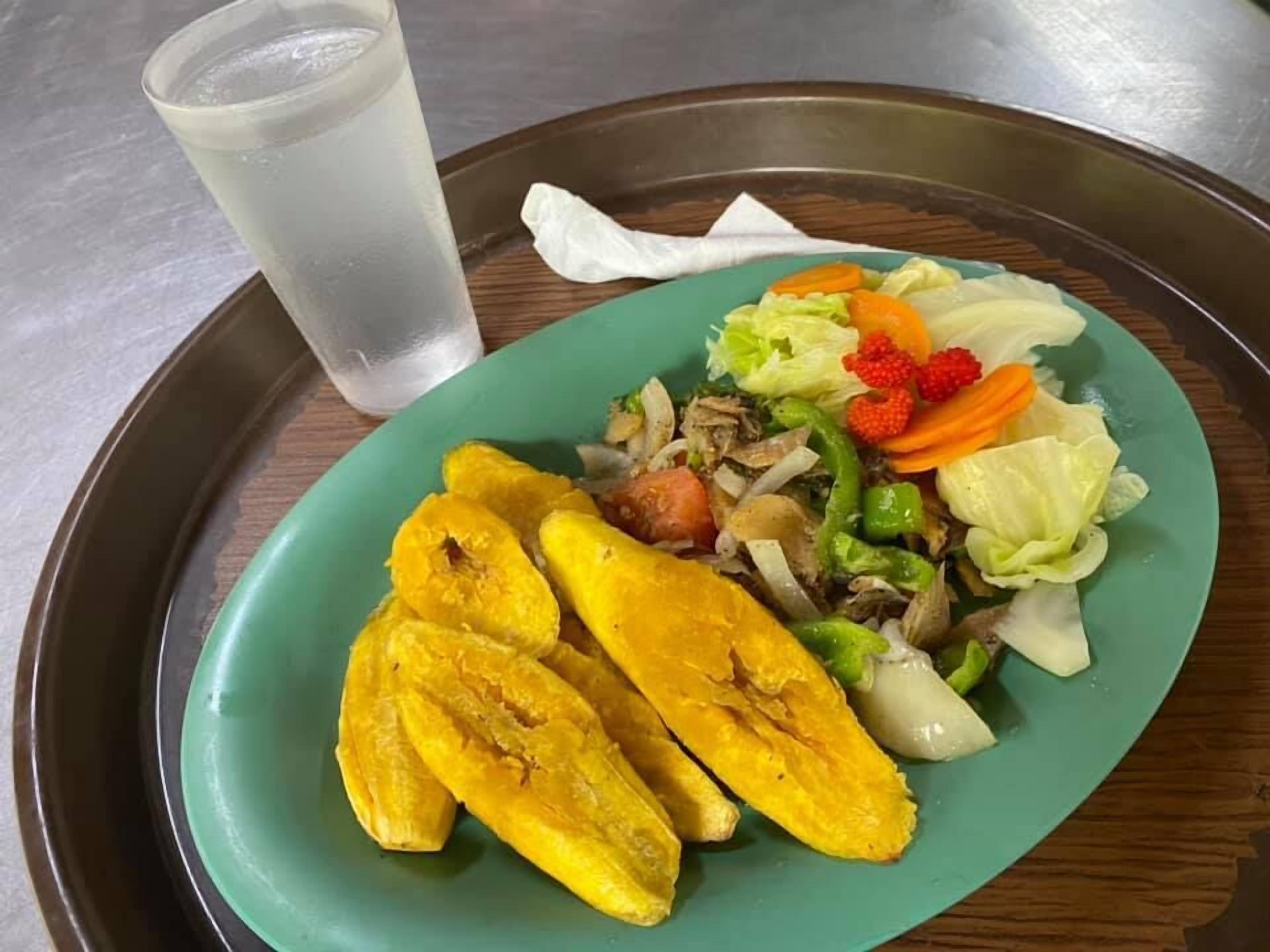 A plate with sliced plantains, vegetables, and a drink on a tray.