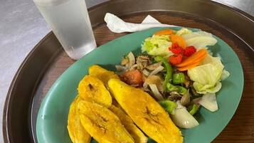 A plate with sliced plantains, vegetables, and a drink on a tray.