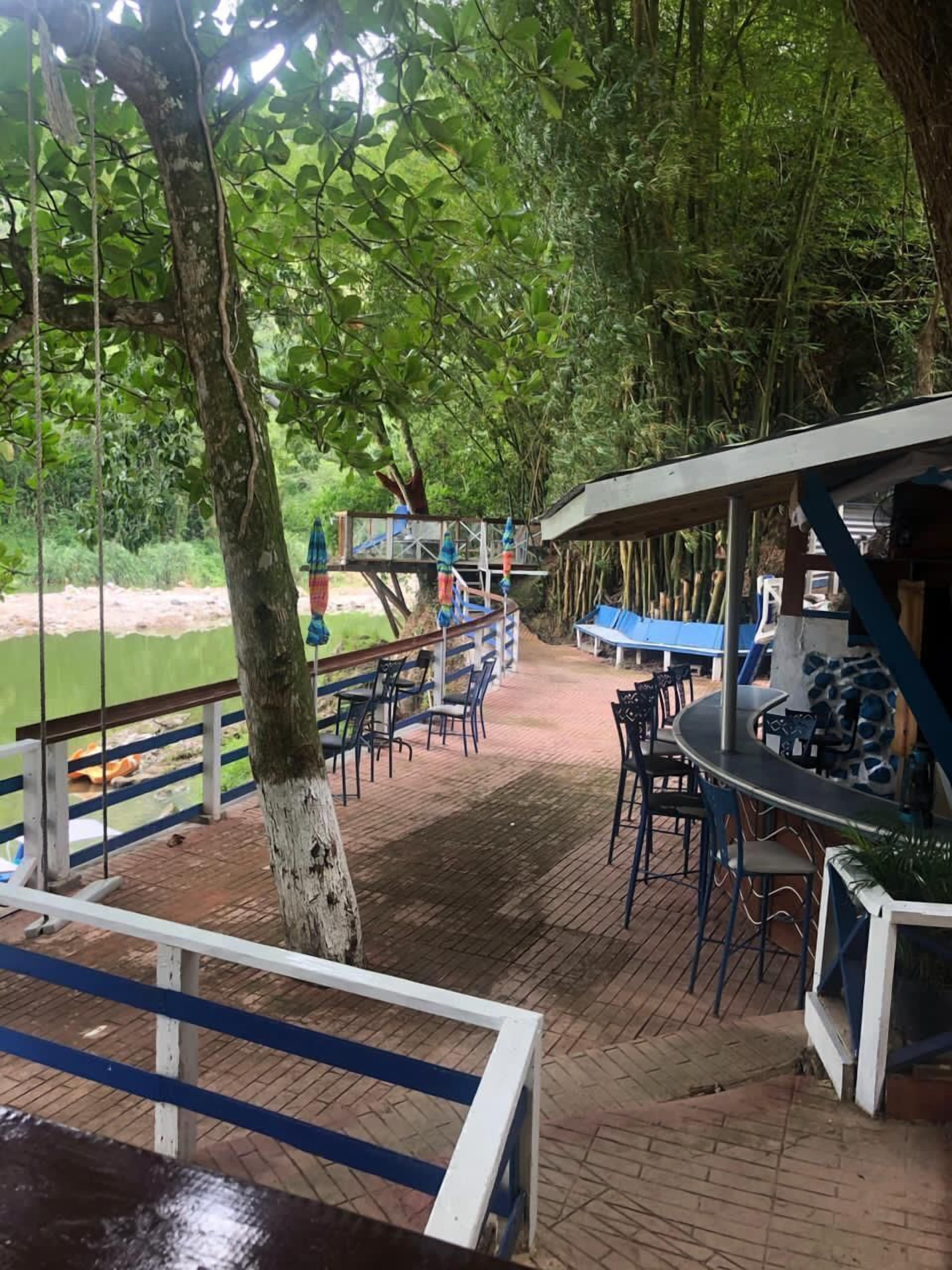 An outdoor patio area with tables and chairs, surrounded by trees and a view of a body of water.