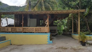 A wooden structure with a covered porch, a concrete floor, and a view of lush greenery and hills in the background. - Tapioca Village Retreat (Castleton)