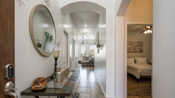A hallway with a mirror, a small table with decorative items, and a bed in the adjacent room. - House with Community Pool and Putting Green (Las Cruces)