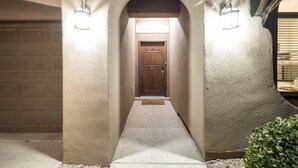 A hallway with a wooden door, two wall-mounted lights, and a welcome mat. - House with Community Pool and Putting Green (Las Cruces)