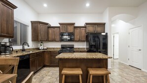 A kitchen with wooden cabinets, granite countertops, a central island with stools, and stainless steel appliances. - House with Community Pool and Putting Green (Las Cruces)