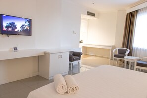 A hotel room with a bed, a TV mounted on the wall, a desk, a chair, and a window with curtains. - Reddoorz Premium @ Bandung City Center (Bandung)