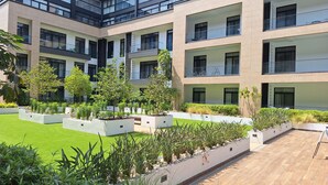 A modern multi-story building with balconies, a well-maintained lawn, and various plants. - Embassy Gardens by Morninglife Luxury (Accra)