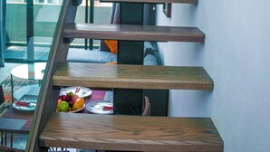 A modern staircase with wooden steps and glass railings, leading to a dining area with a table set for two. - Embassy Gardens by Morninglife Luxury (Accra)