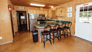 Une cuisine de style rustique, avec des éléments en bois, comprenant un îlot central, des tabourets de bar, un réfrigérateur, un four à micro-ondes et un évier.