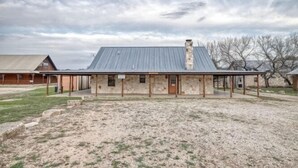 Un bâtiment rustique avec un toit en métal et des murs en pierre, un espace extérieur couvert et un champ verdoyant au premier plan.