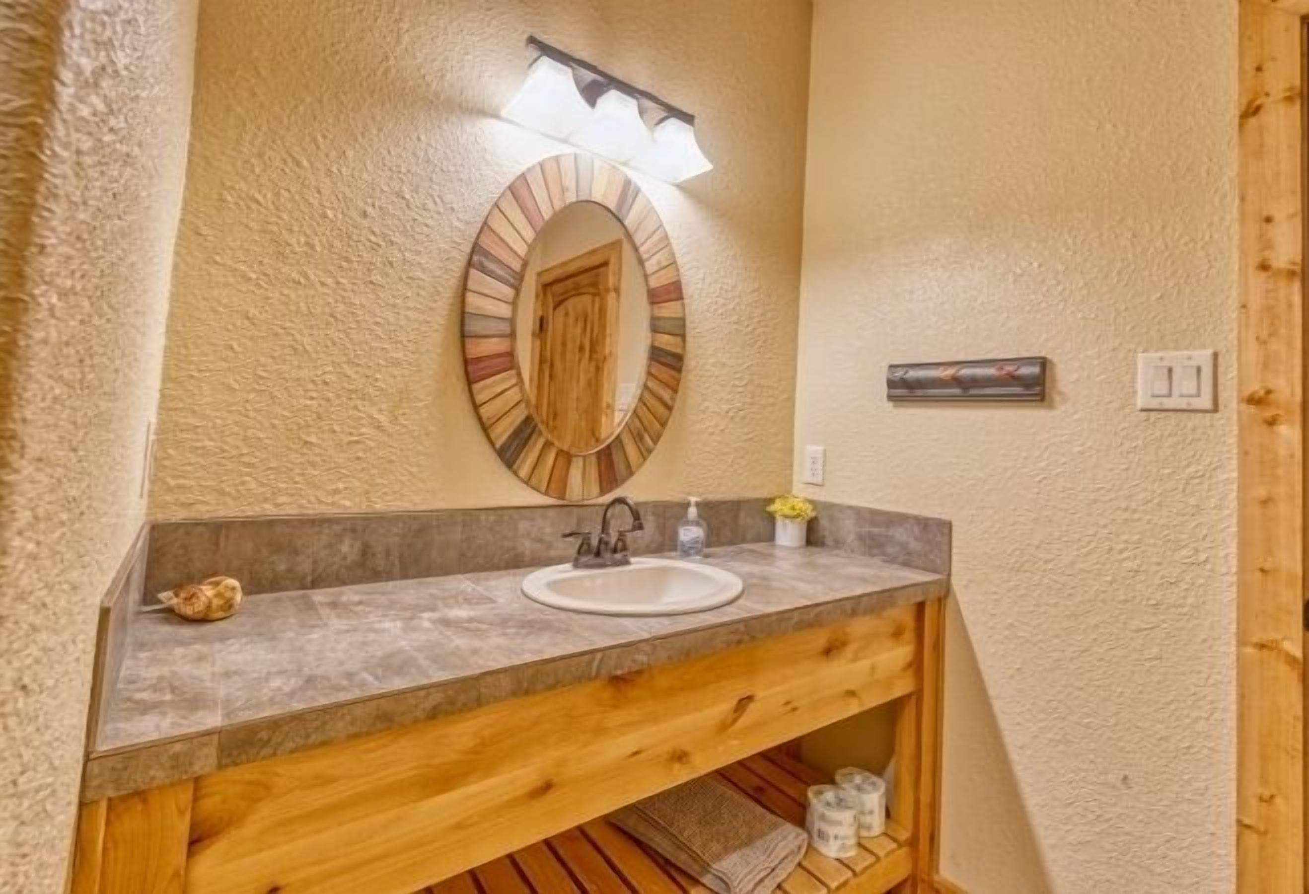 Une salle de bain avec un meuble-lavabo en bois, un miroir rond, un évier et un porte-serviettes.