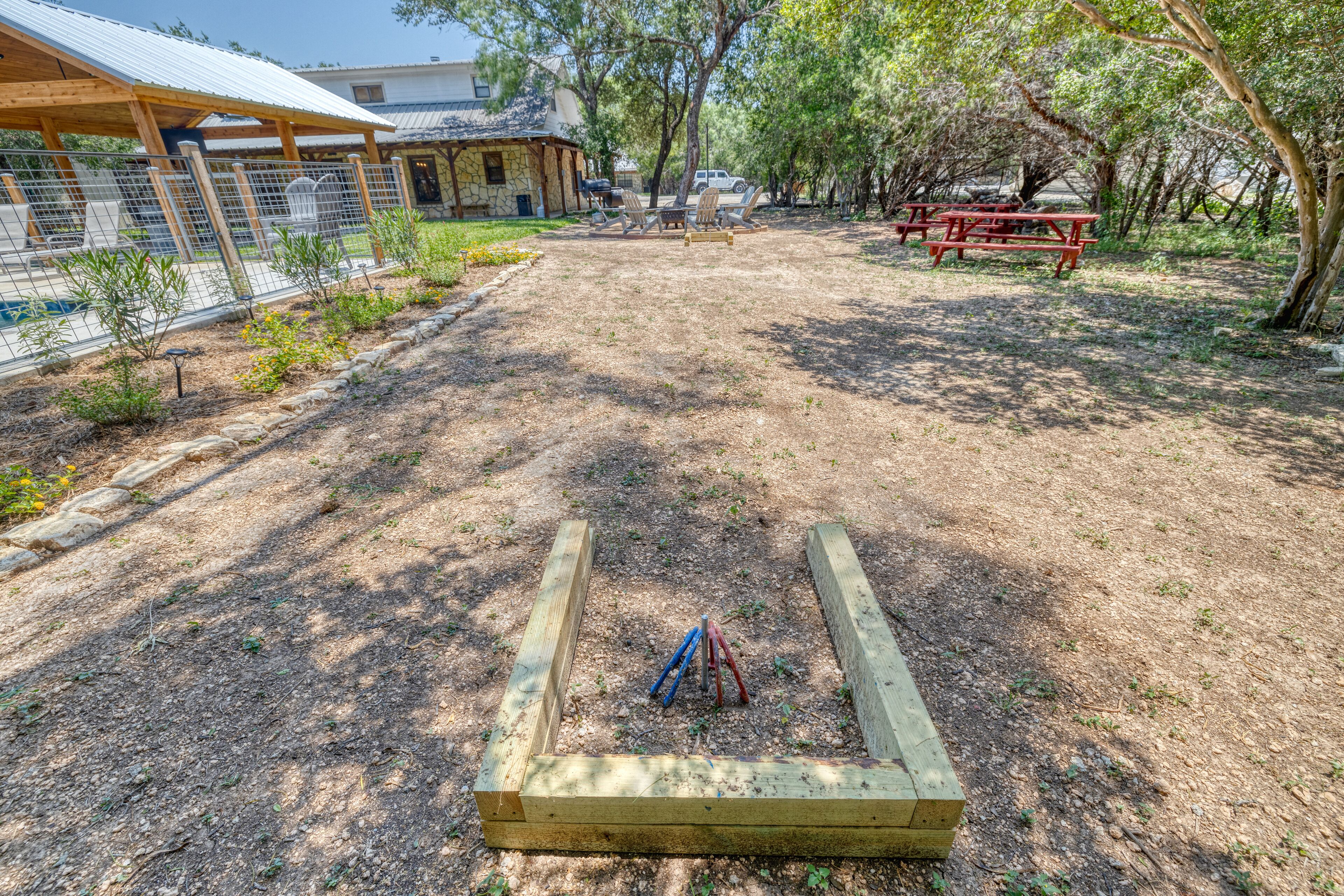 A fenced outdoor area with a picnic table and chairs, a wooden play structure, and a stone building in the background.