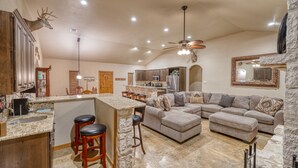 A spacious living area with a large sectional sofa, a kitchen with granite countertops, and a stone accent wall. - Beautiful and spacious home with a pool (Concan)