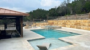 A swimming pool with a hot tub, stone walls, and a covered seating area. - Beautiful and spacious home with a pool (Concan)