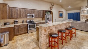 A kitchen with wooden cabinets, granite countertops, a stone island with stools, a deer head mounted on the wall, and a fireplace. - Beautiful and spacious home with a pool (Concan)