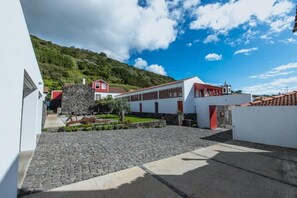 A courtyard with a stone pathway, a white building with red accents, and a hill in the background.