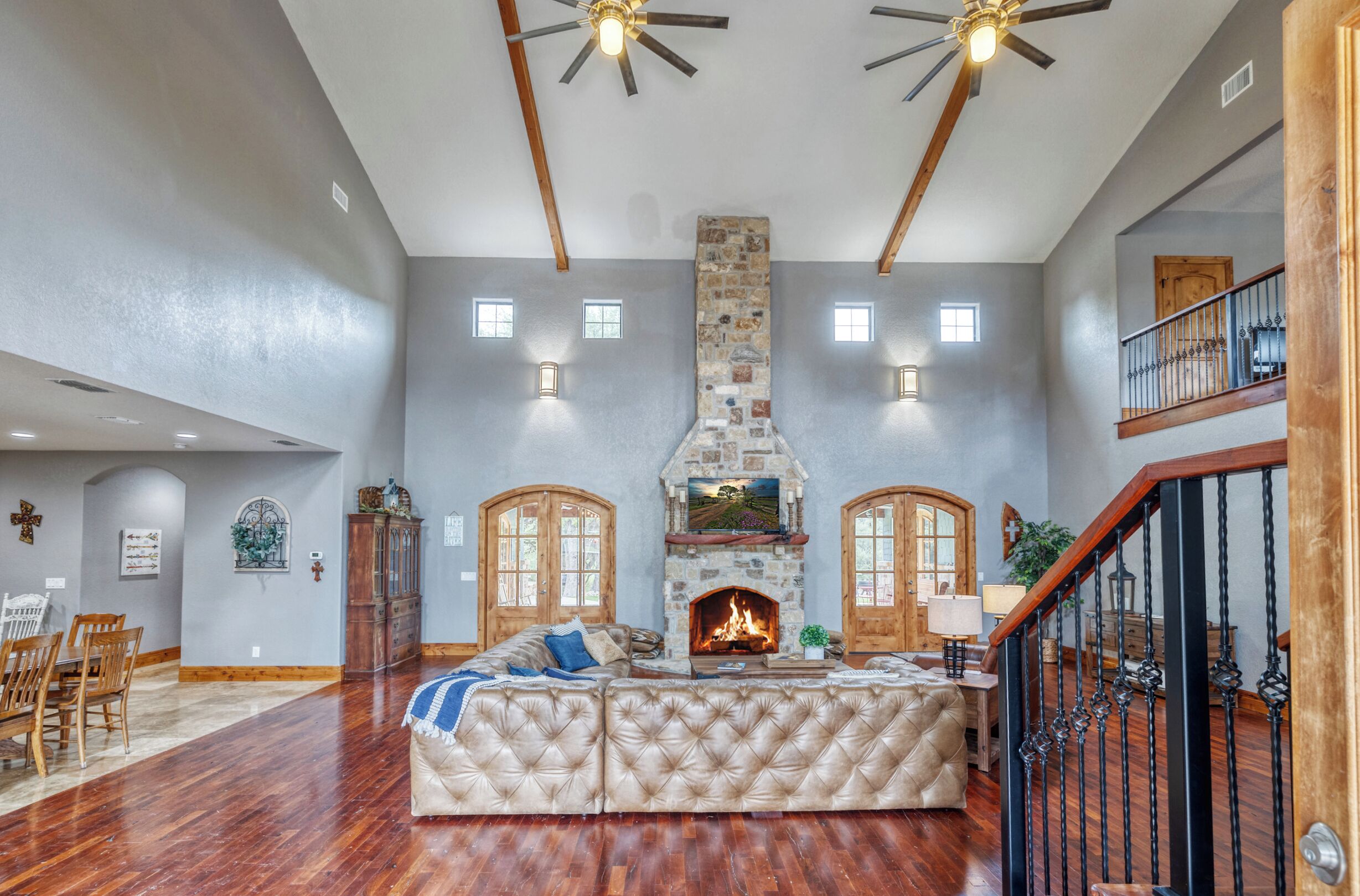 A spacious living room with a fireplace, wooden flooring, and a high ceiling with exposed beams.