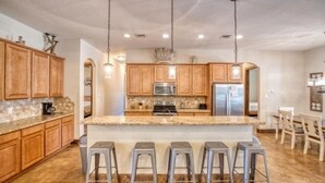 A kitchen with wooden cabinets, a granite countertop, a central island with bar stools, stainless steel appliances, and pendant lighting. - Heartstone Subdivision with a pool (Concan)