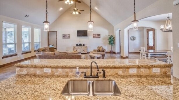 A spacious kitchen with granite countertops, a double sink, pendant lighting, and a high ceiling with a fan. - Heartstone Subdivision with a pool (Concan)