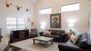Een woonkamer met een bruine leren bank, een houten salontafel, een open haard en aan de muur bevestigde hertenkoppen.