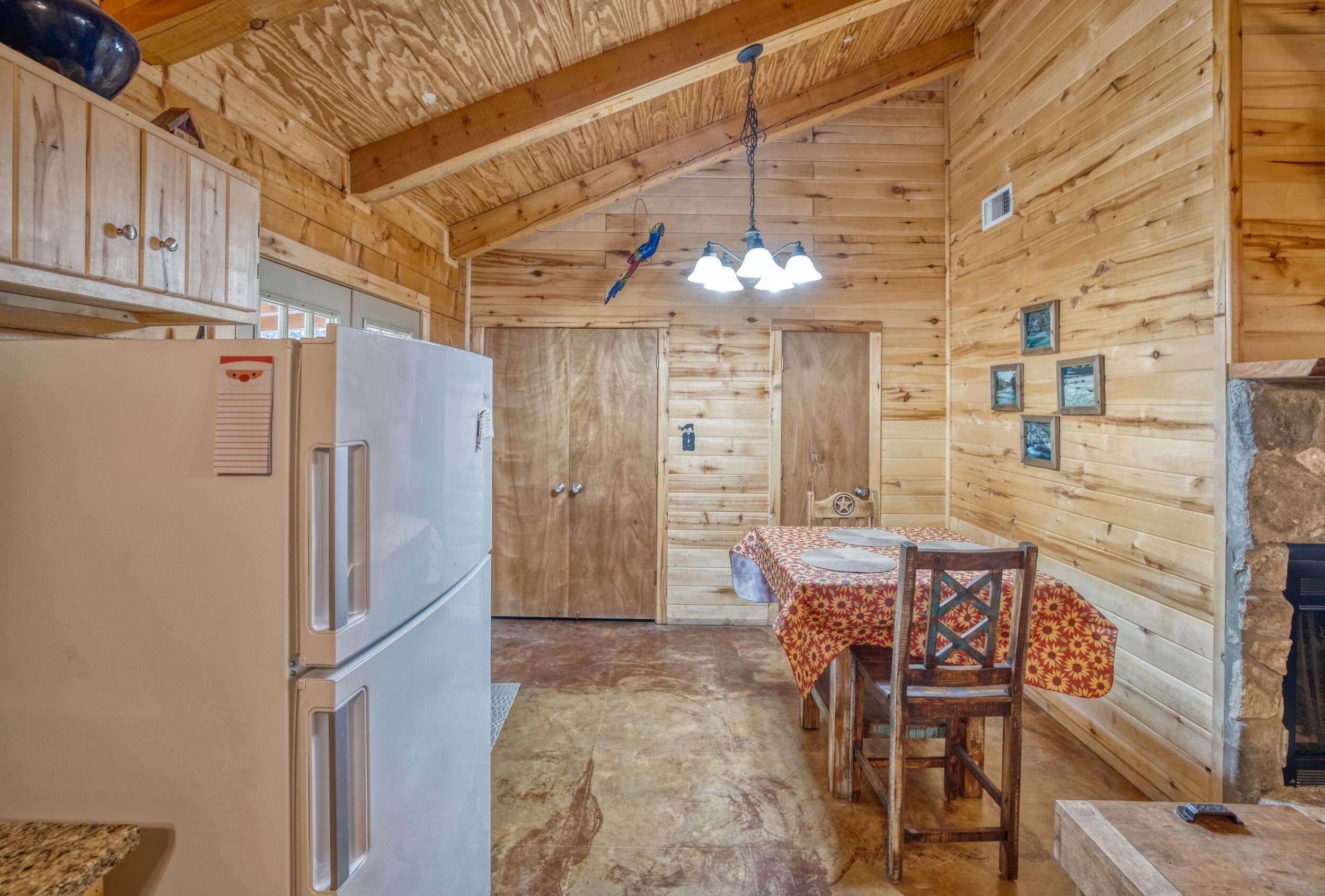 El interior de una cabaña de madera con cocina, que incluye un refrigerador, armarios de madera y una mesa de comedor con sillas.