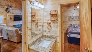 A wooden cabin interior with a bathroom, a bed, and a television. - Beautiful home in the Comanche Crossing Subdivision (Concan)