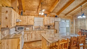 A wooden cabin-style kitchen with granite countertops, wooden cabinets, a central island with seating, and a ceiling fan. - Beautiful home in the Comanche Crossing Subdivision (Concan)
