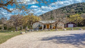 A stone building with a wooden door, surrounded by a gravel driveway and trees. - Beautiful home in the Comanche Crossing Subdivision (Concan)