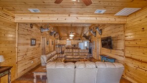 A log cabin interior with a leather sectional sofa, a kitchen area, and mounted deer heads on the walls. - Beautiful home in the Comanche Crossing Subdivision (Concan)