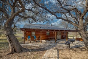 A rustic log cabin with a porch, benches, and a grill area.