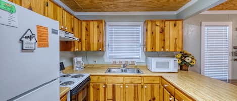 A kitchen with wooden cabinets, a white refrigerator, a stove, a microwave, and a sink.