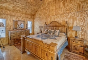 Une chambre à coucher avec une tête de lit en bois, un lit recouvert d’une courtepointe, une table de chevet, une commode et un miroir.