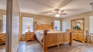 A bedroom with a wooden bed, nightstands, a dresser, a ceiling fan, and a large mirror. - Large river front home in Cypress Bend (Concan)