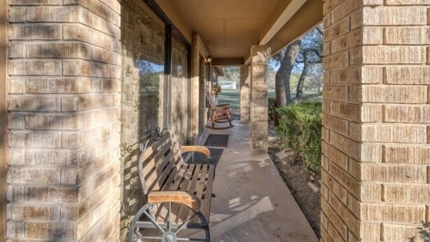 A covered walkway with benches and a rocking chair, bordered by brick walls and glass doors. - Small home in a quiet neighborhood (Concan)