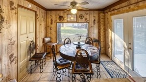 A wooden-paneled room with a round table and chairs, a ceiling fan, and a large window. - Small home in a quiet neighborhood (Concan)
