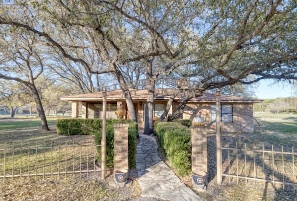 A house with a stone pathway leading to a wooden gate, surrounded by trees and a fenced yard.
