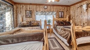 A rustic cabin room with two wooden beds, a ceiling fan, and wooden walls. - Small home in a quiet neighborhood (Concan)