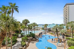A resort pool area with palm trees, a water slide, and a view of the ocean. - Sunset Balcony View | Beachfront | Great Location (Panama City)