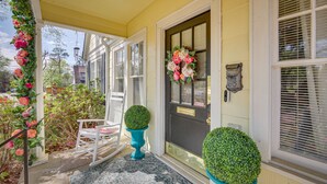 A porch with a rocking chair, a door with a wreath, and potted plants. - 'The Pink Azalea' - Tyler Home w/ Yard + Patio! (Tyler)