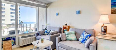 A living room with two grey sofas, a small white table, and a view of the ocean through large windows.