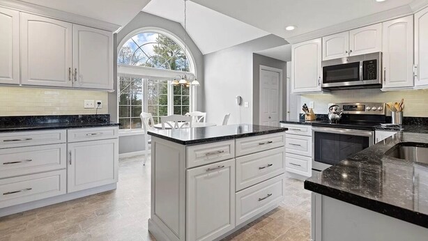 A modern kitchen with white cabinetry, a large island with a black countertop, and a built-in microwave. - Close to Wequaquet Lake, beautiful and spacious cottage (Barnstable)