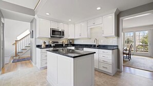 A modern kitchen with white cabinetry, a central island, and a large window providing natural light. - Close to Wequaquet Lake, beautiful and spacious cottage (Barnstable)