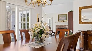 A dining room with a wooden table, chairs, a vase of white flowers, a chandelier, and a fireplace. - Close to Wequaquet Lake, beautiful and spacious cottage (Barnstable)